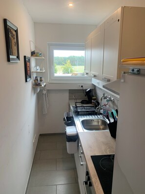 A compact kitchen with a window, white cabinets, and a built-in oven. - Zimmer Adelheid (Adelheidsdorf)