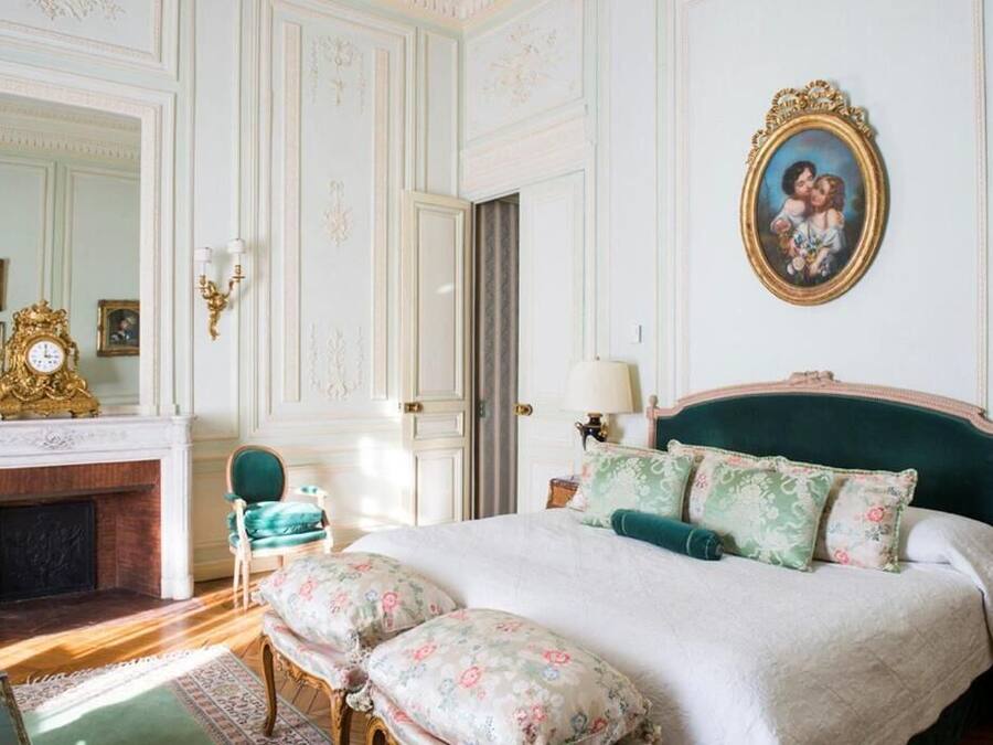 Une chambre à coucher classique avec un grand lit, une commode, un miroir et une cheminée.