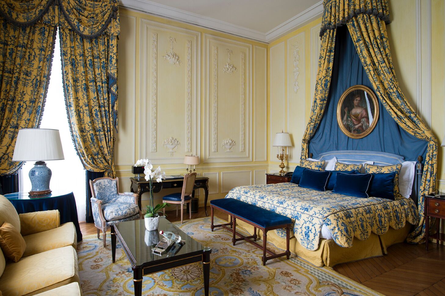 A classic, elegantly furnished bedroom with a canopy bed, a desk, and a comfortable seating area.