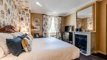 A hotel room with a large bed, a fireplace, a television, and a mirror.