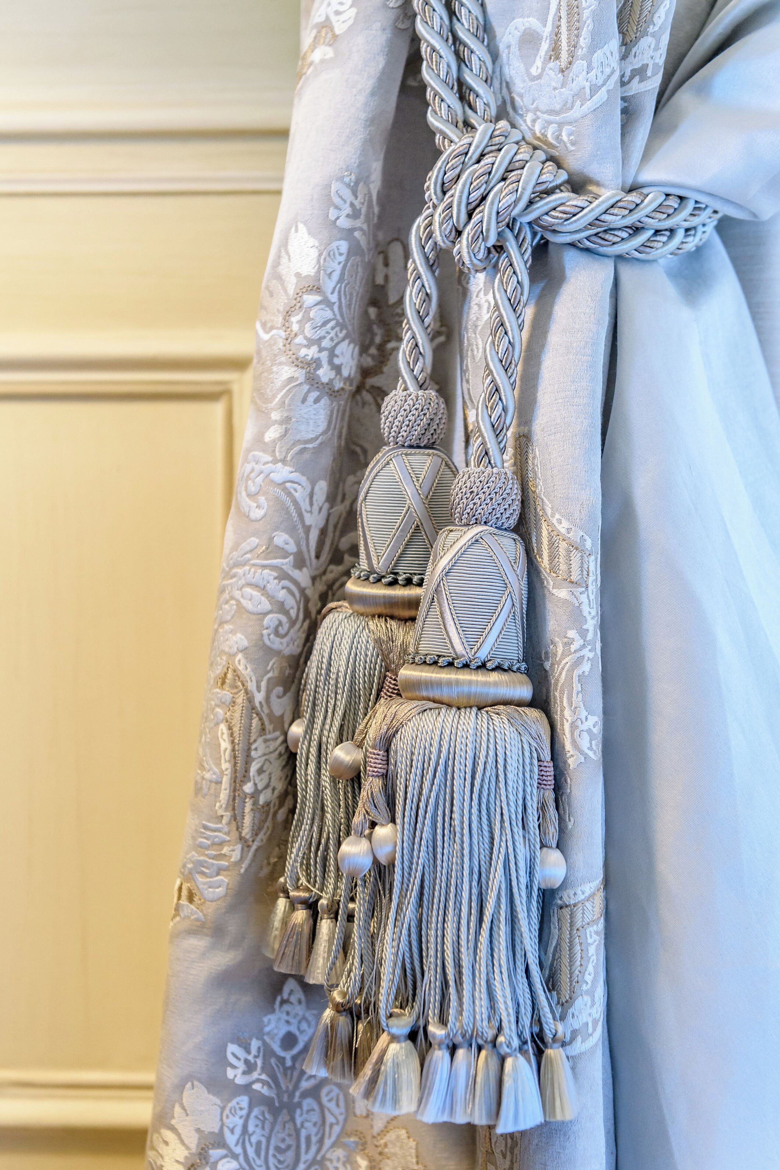 A curtain with a decorative tassel and a braided tie.