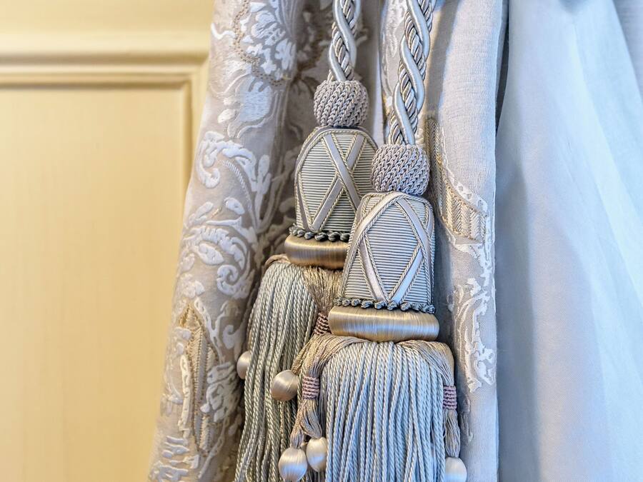 A curtain with a decorative tassel and a braided tie.