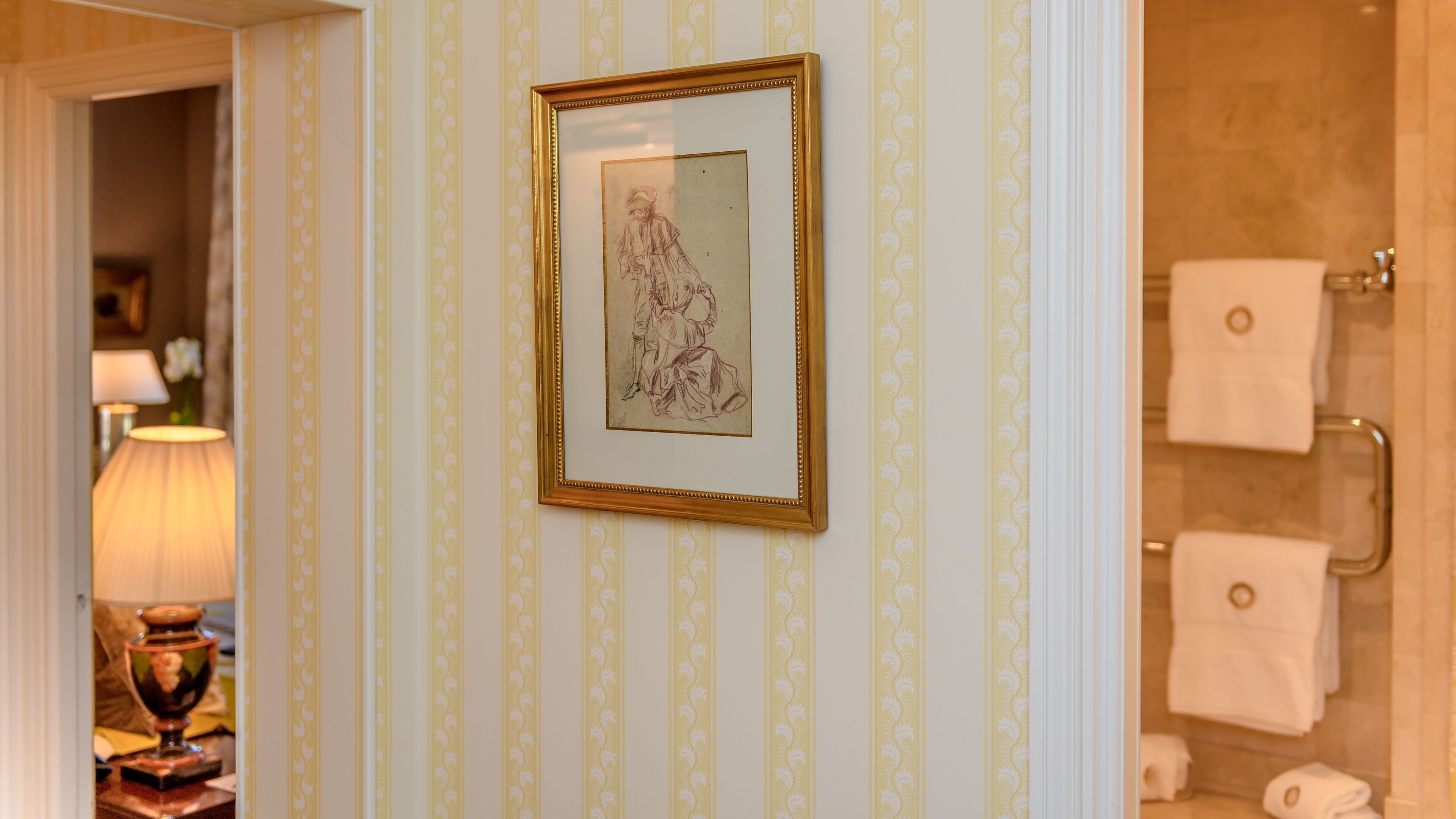 A bathroom with striped wallpaper, a framed artwork on the wall, and a towel rack with towels.
