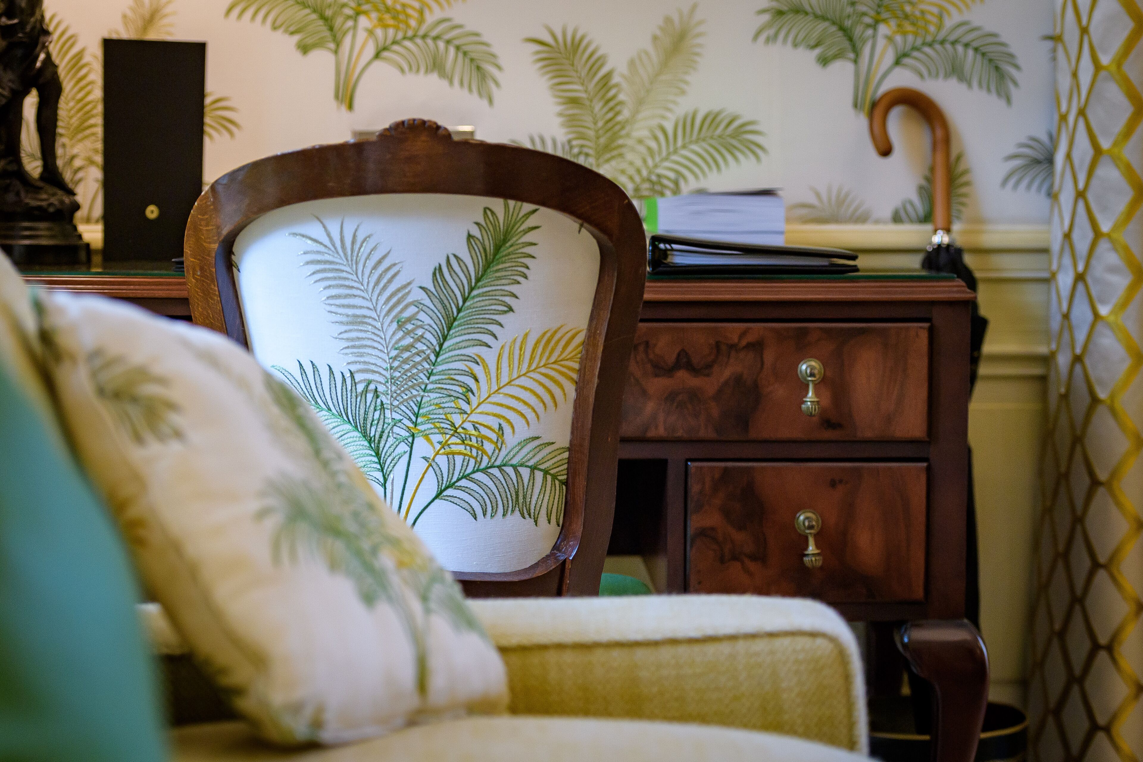 A room with a wooden chair featuring a leaf pattern, a wooden cabinet with drawers, and a patterned wall.