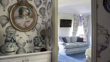 Una habitación con papel tapiz estampado, un retrato enmarcado, un sofá y un televisor.