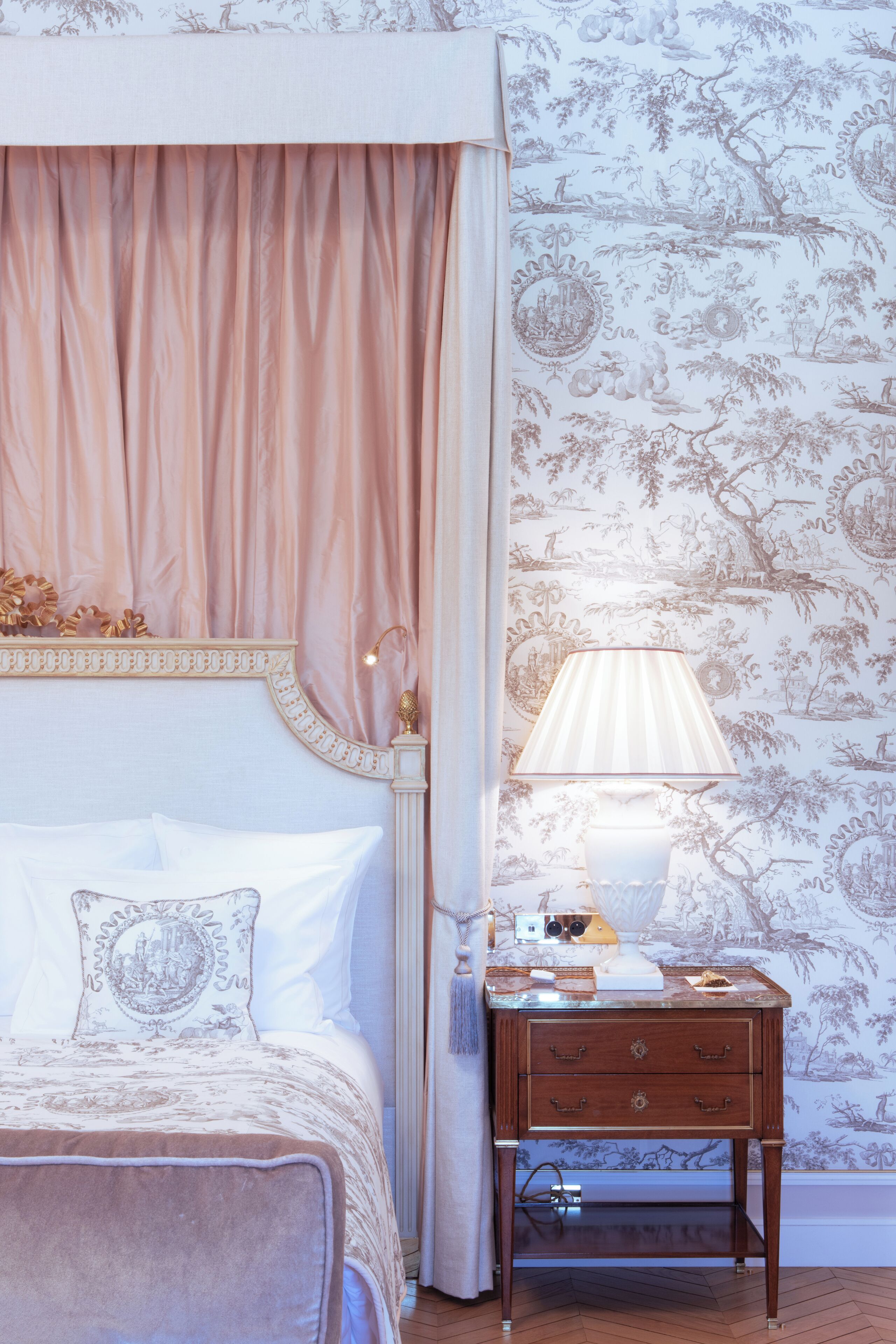 Une chambre à coucher avec un lit à baldaquin, une table de chevet avec une lampe et un papier peint à motifs floraux.