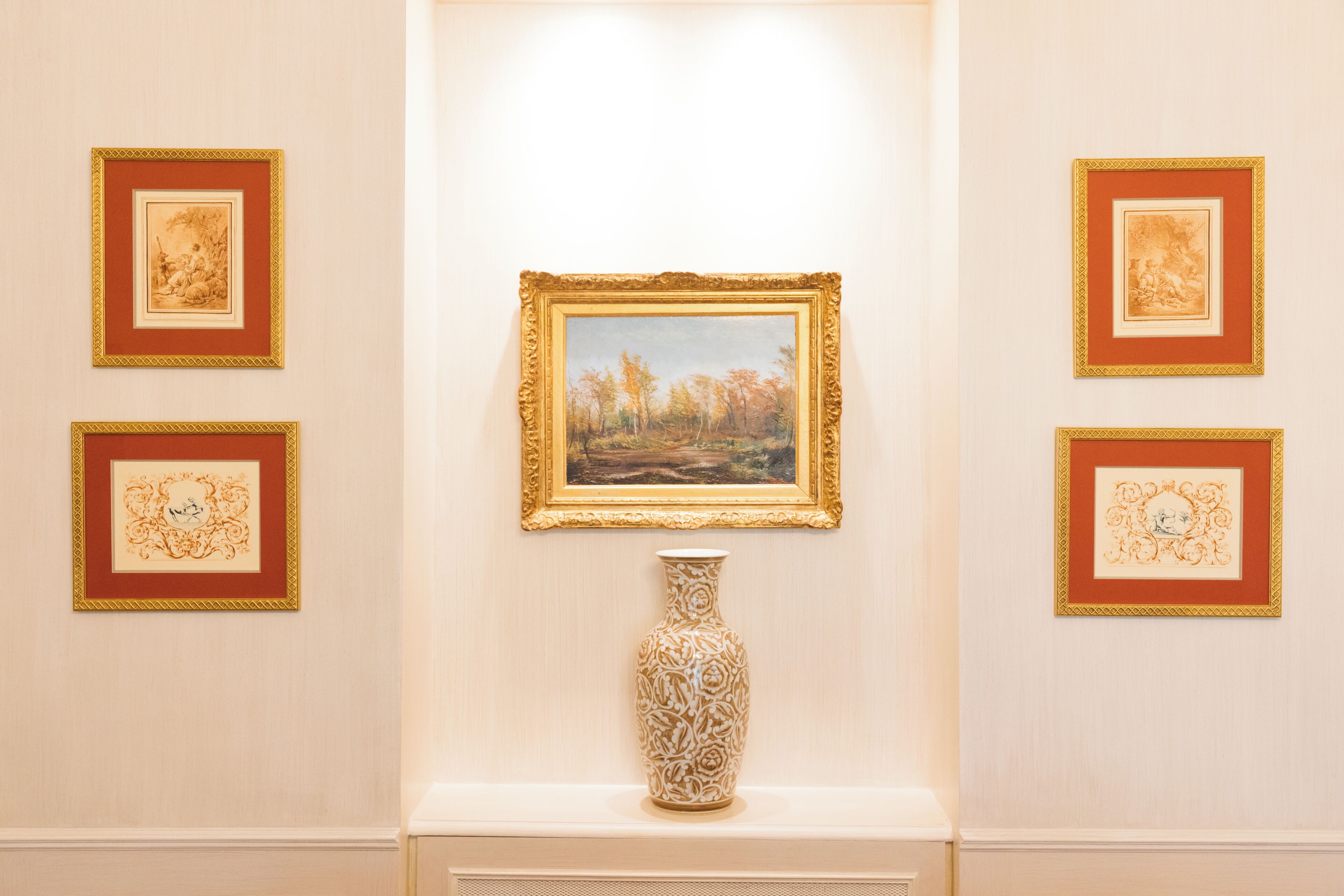 Una pared de galería con obras de arte enmarcadas y un jarrón decorativo.