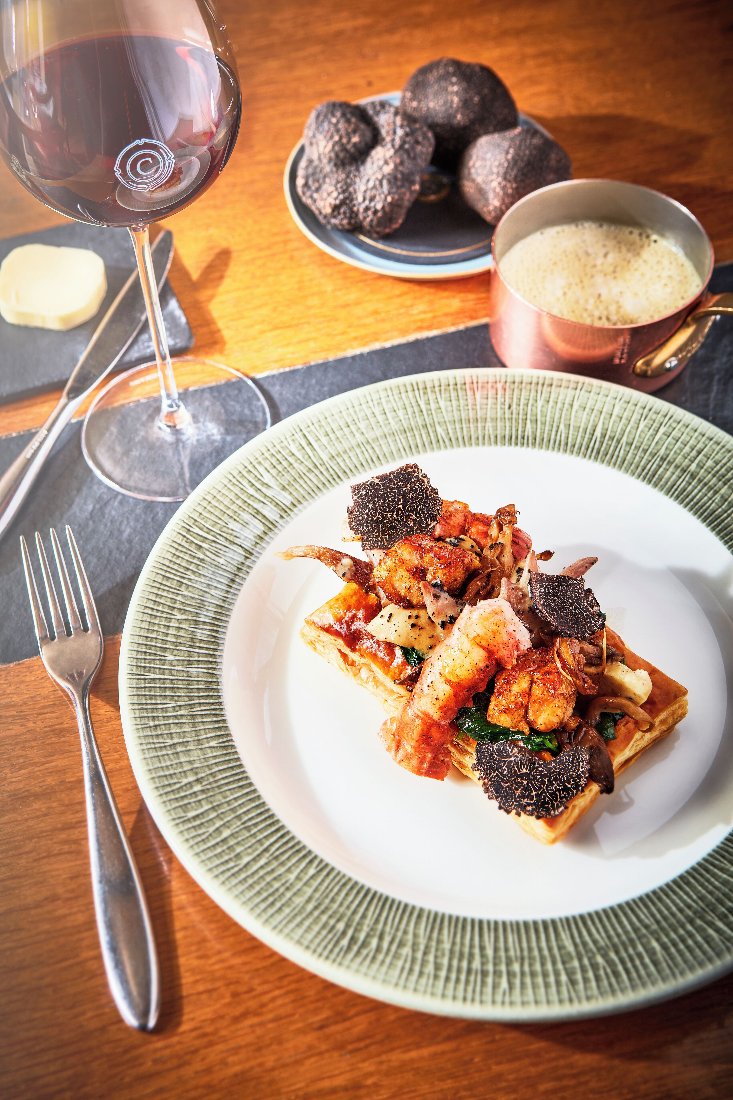 A plate of food with a glass of red wine and a bowl of truffles on a wooden table.