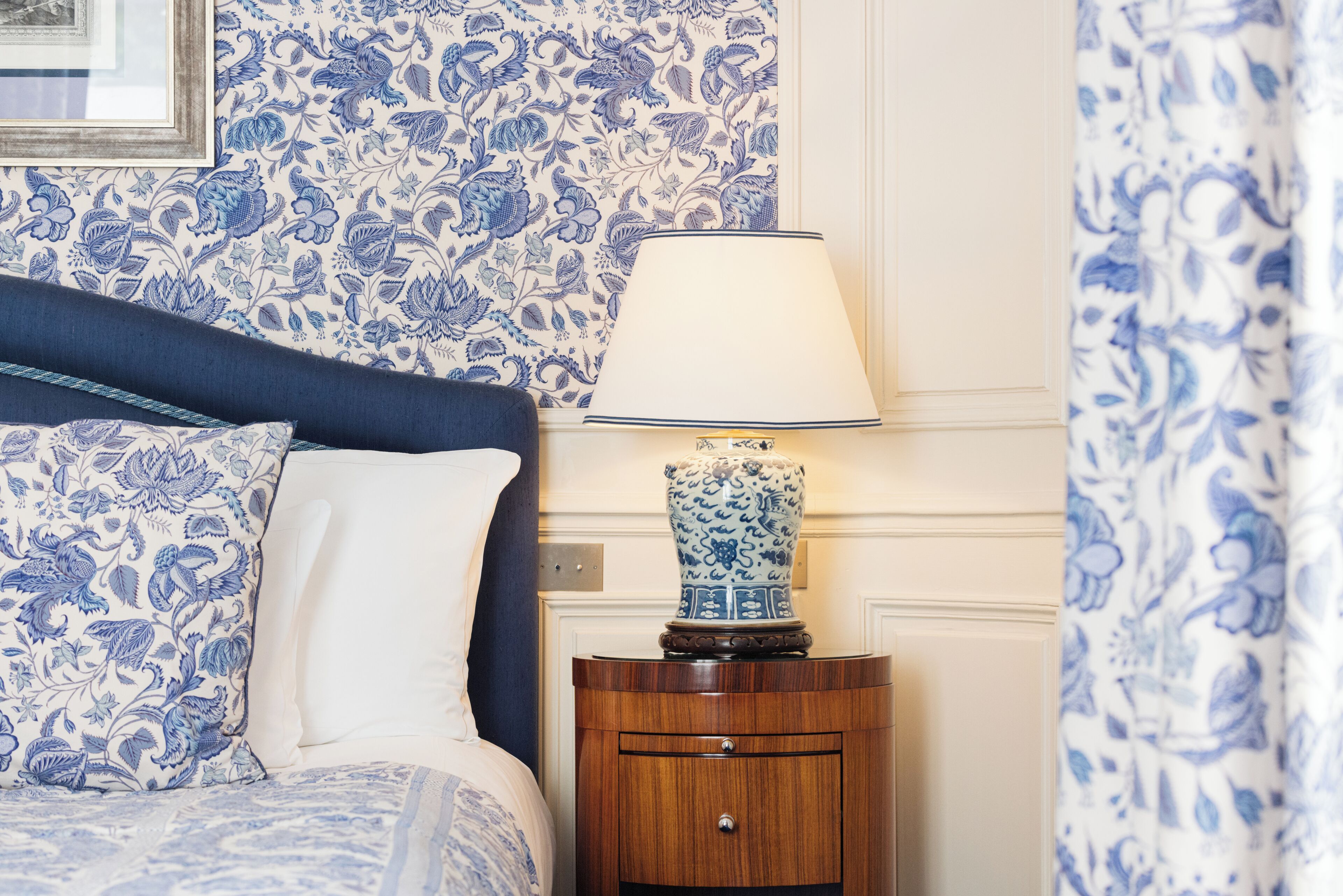 A bedroom with a bed, a nightstand with a lamp, and floral wallpaper.