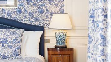 A bedroom with a bed, a nightstand with a lamp, and floral wallpaper.