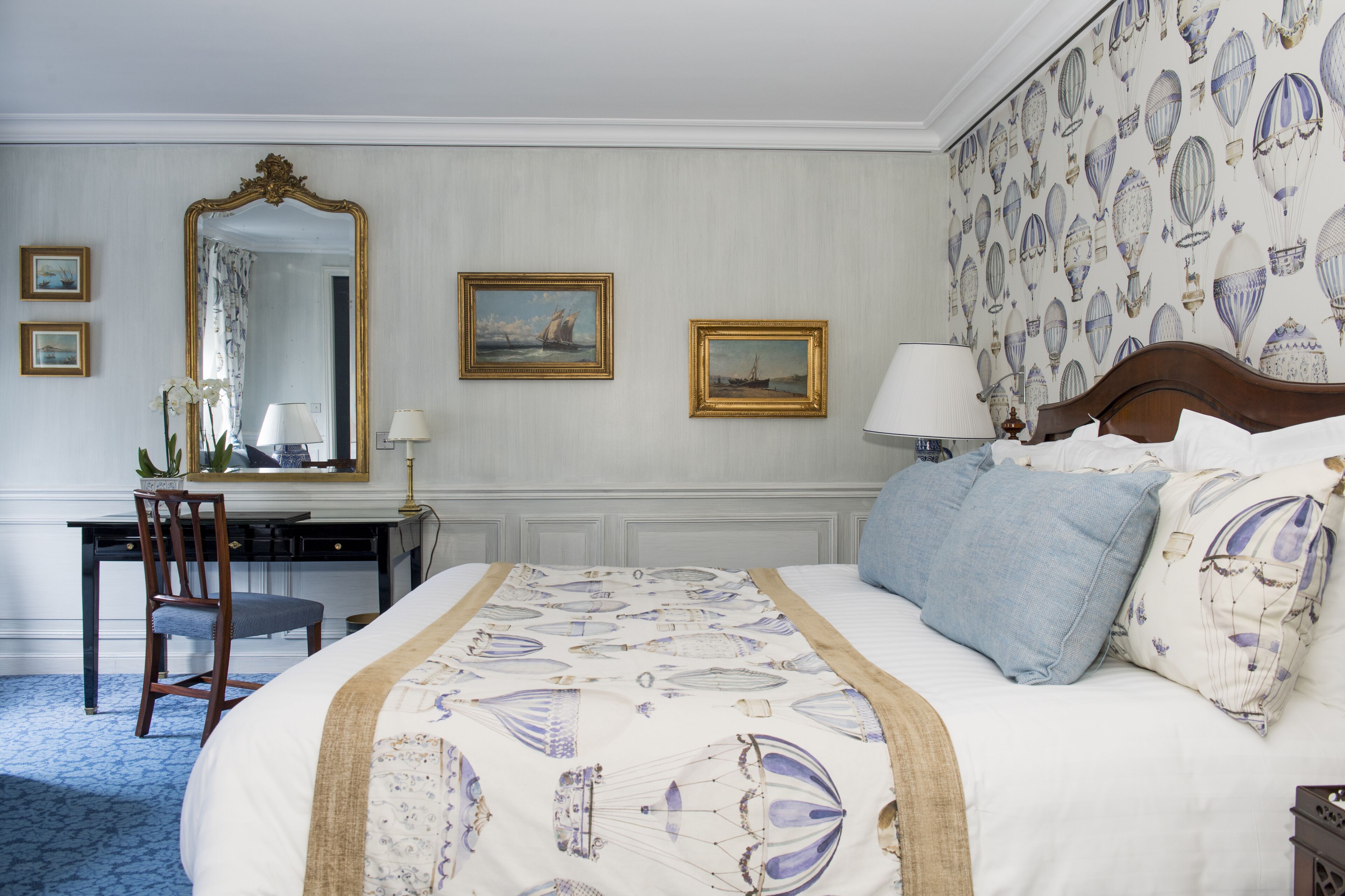 Habitación de hotel con una cama grande, un escritorio, una silla, un espejo y cuadros en la pared.