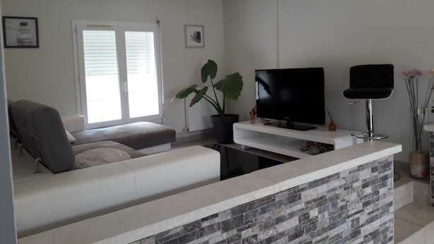 Una sala de estar moderna con un sofá, un televisor de pantalla plana, una mesa de centro y una pequeña zona de bar con protector de piedra.