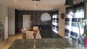 Una sala de estar moderna con comedor, que incluye una amplia mesa de mármol, cortinas blanco y negro y una lámpara colgante negra.