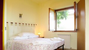 Une chambre à coucher avec un lit, une table de chevet avec une lampe, une fenêtre donnant sur un paysage verdoyant et un radiateur.