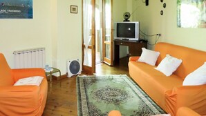 Un salon avec un canapé orange, un téléviseur posé sur un meuble en bois, un ventilateur et un tapis à motifs.