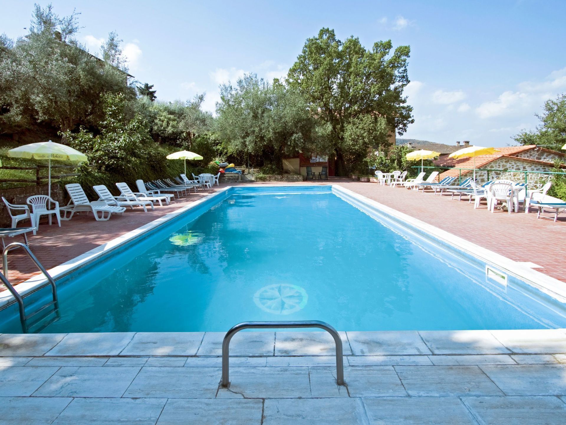 Ein Swimmingpool mit Liegestühlen und Sonnenschirmen, umgeben von Bäumen und einer Steinmauer.