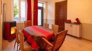 Ein gemütlicher Raum mit Esstisch, Korbstühlen, einer rot-grauen Tischdecke, einem roten Heizgerät, einer Tür und einer kleinen Küchenzeile mit einem roten Toaster.