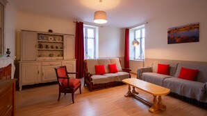 Ein Wohnzimmer mit Holzboden, einer Sofagarnitur, einem Esstisch und einem Schrank mit Geschirr.