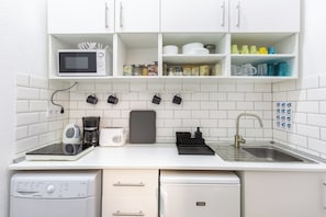Compact kitchen with modern design, equipped with microwave, coffee maker, and dishwasher, plus hanging mugs and a sink.