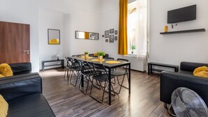 Un salon moderne avec un coin repas, comprenant un canapé, une table à manger avec des chaises, un téléviseur fixé au mur et une fenêtre avec des rideaux.