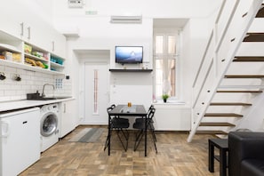 Enjoy a compact apartment with a modern kitchen, dining area, and flat-screen TV, plus a staircase leading to an upper level.