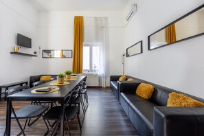 A modern living room with a black leather sofa, a dining table with chairs, a flat-screen TV, and a large window with curtains. - ⭐7ROOM-15BED-4BATH ☕FREE-BEER & BREAKFAST ❤️AIRCO (VIII. kerület)