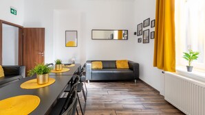Een moderne woonkamer met een zwarte leren bank, gele kussens, een eettafel met stoelen en een potplant.