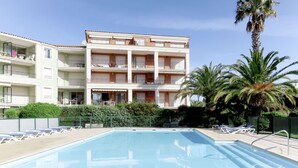 Uma área de piscina com espreguiçadeiras e um edifício com várias varandas.