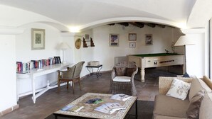 Ampla sala de estar com mesa de bilhar, sofá, mesinha de centro com revistas e estante de livros.