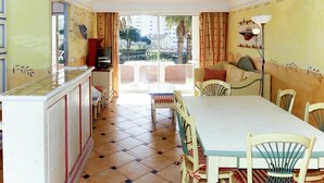 Uma área de refeições com mesa e cadeiras, uma televisão e uma varanda com vista para edifícios e árvores.