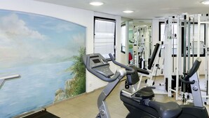 Una palestra con macchinari cardio, attrezzature per l'allenamento con i pesi e un murale raffigurante una veduta costiera.