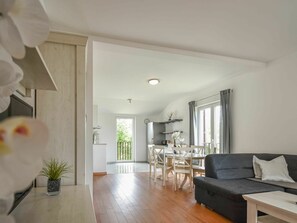 Ein modernes Wohnzimmer mit einem dunkelgrauen Sofa, einem Holzesstisch mit Stühlen und einer Küche im Hintergrund.