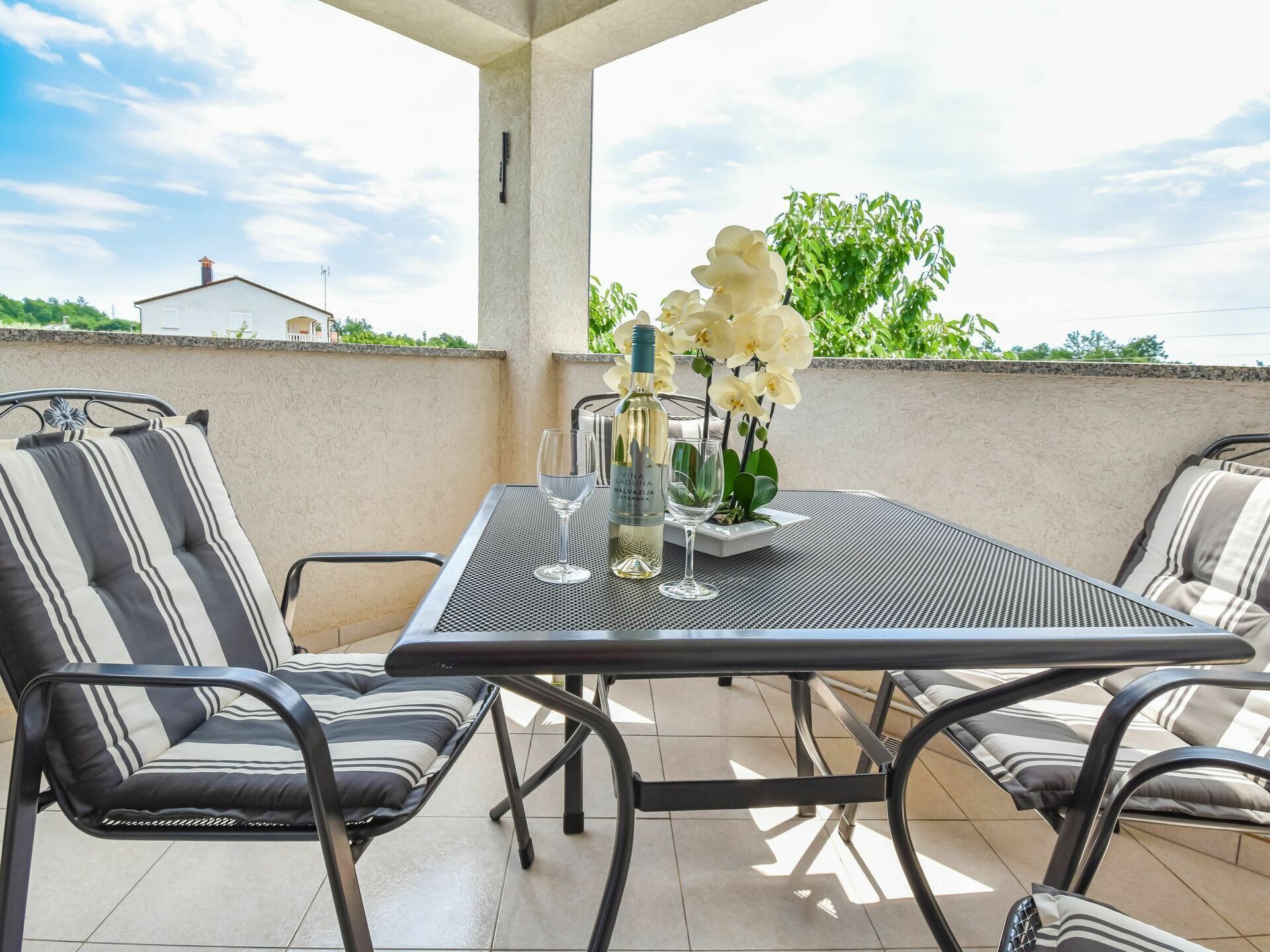 A patio with a table and chairs, a bottle of wine, and a vase of flowers.