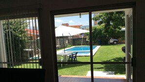 Vista a través de un ventanal corredero a un patio trasero con piscina, césped y zona de patio.