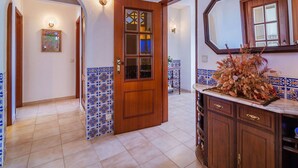 Een gang met een houten deur, betegelde muren en een badkamer met een houten wastafel en spiegel.