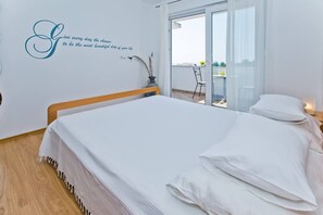 A bedroom with a bed, a wall with a quote, and a balcony with a chair. - Apartments Nina Hvar town (Hvar)