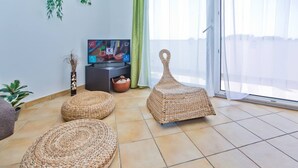 A living room with a TV, two woven poufs, a plant, and a large window with curtains. - Apartments Nina Hvar town (Hvar)