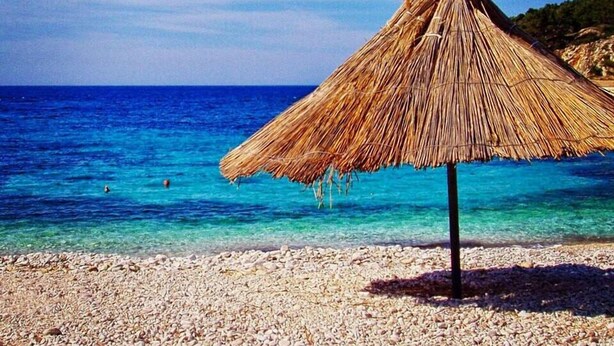 A beach with a thatched umbrella and clear blue water. - Apartments Nina Hvar town (Hvar)