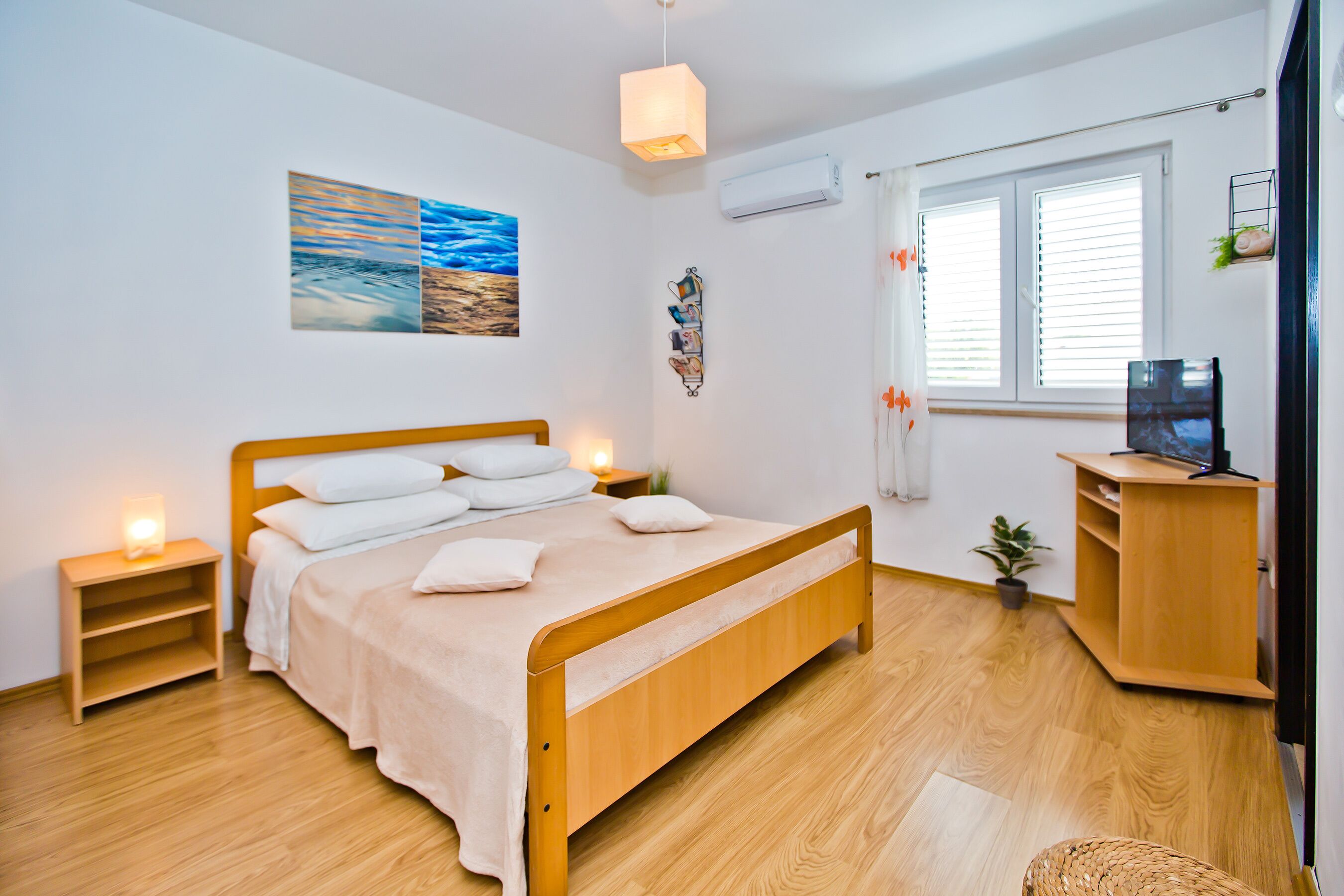 A bedroom with a wooden bed, bedside tables, a wall-mounted TV, and a window with blinds.