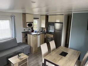 Compact kitchenette with microwave, stove, and refrigerator, adjacent to a living area with dining table and sofa.