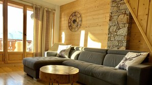 Un salón acogedor con un sofá seccional, una mesa de centro redonda de madera y una pared de piedra.