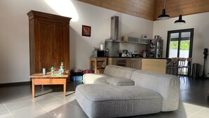 A spacious living area with a large grey sectional sofa, a wooden cabinet, and a kitchen in the background. - Villa with pool, close to beaches and town center. (Narbonne)