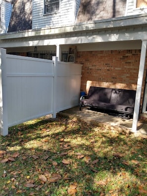 A covered patio area with a white fence, a brick wall, and a black outdoor sofa.