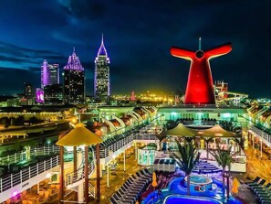 A cruise ship deck with a large red funnel, a pool area, and a view of the city skyline in the background. - Valerie's  Victoria's Small Apartment #1 (Mobile)