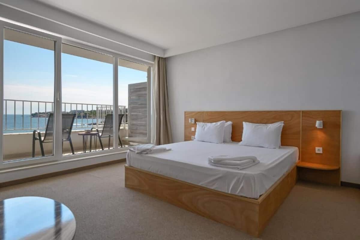 Una habitación de hotel con una cama grande, vista al mar y un balcón con sillas.