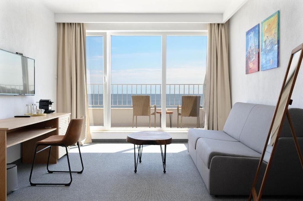 Habitación de hotel con balcón, sofá, escritorio y dos sillas.