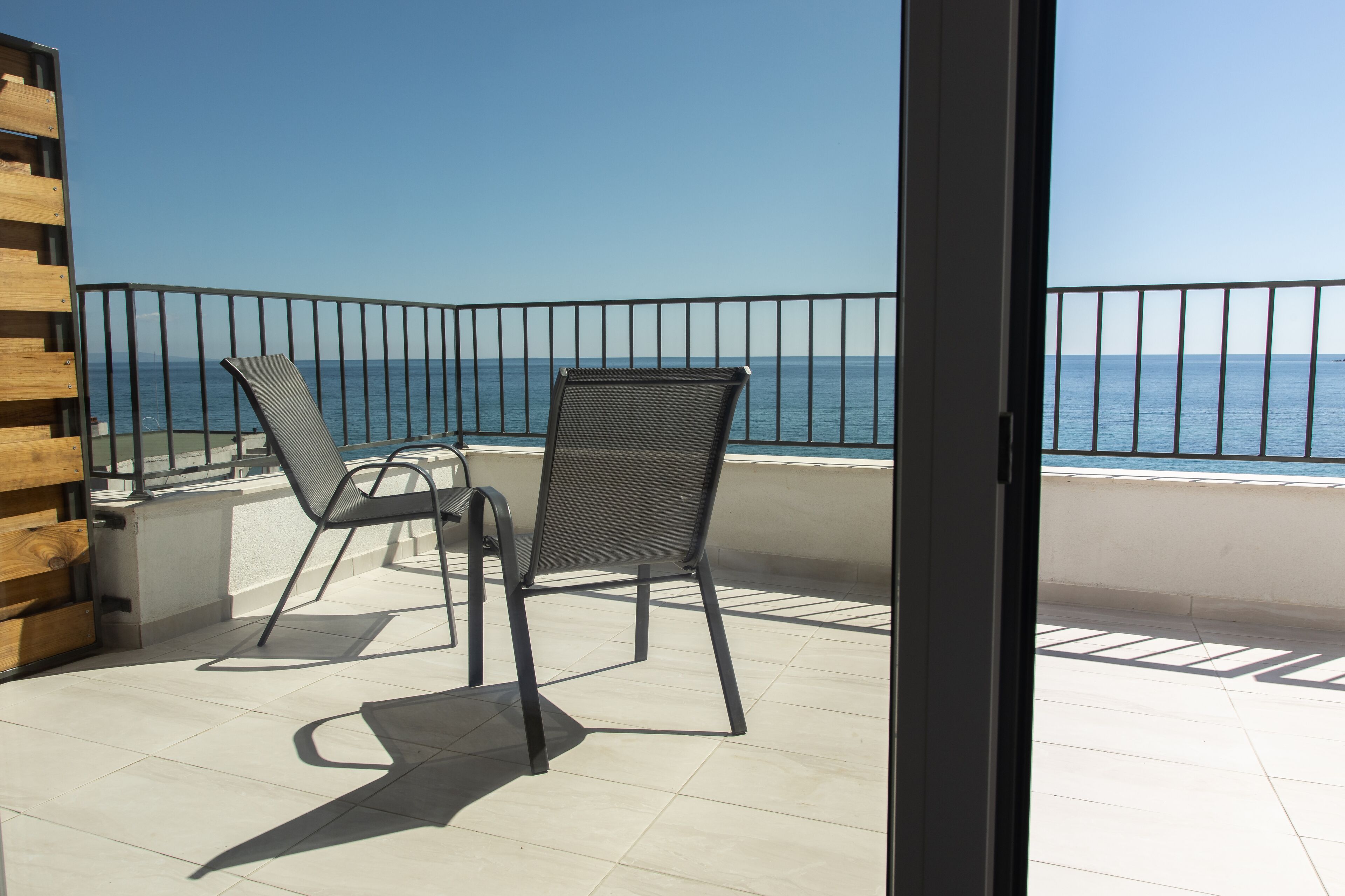 A balcony with two chairs, a wooden bench, and a view of the sea.