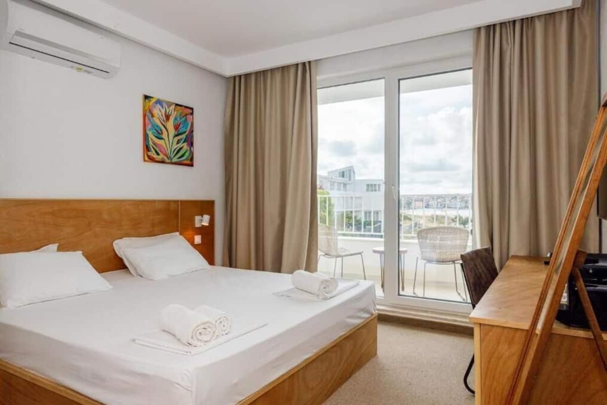 Una habitación de hotel con una cama grande, un escritorio, una silla, un cuadro en la pared y vistas a la ciudad a través de la ventana.