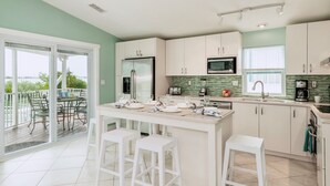 A modern kitchen with white cabinets, a central island with bar stools, a dining area with a view of the outdoors, and a balcony with outdoor furniture. - **TIDEWATER VIEWS** Cottage + Boat Slip + Pool + Last Key White Glove Service... (Cudjoe Key)