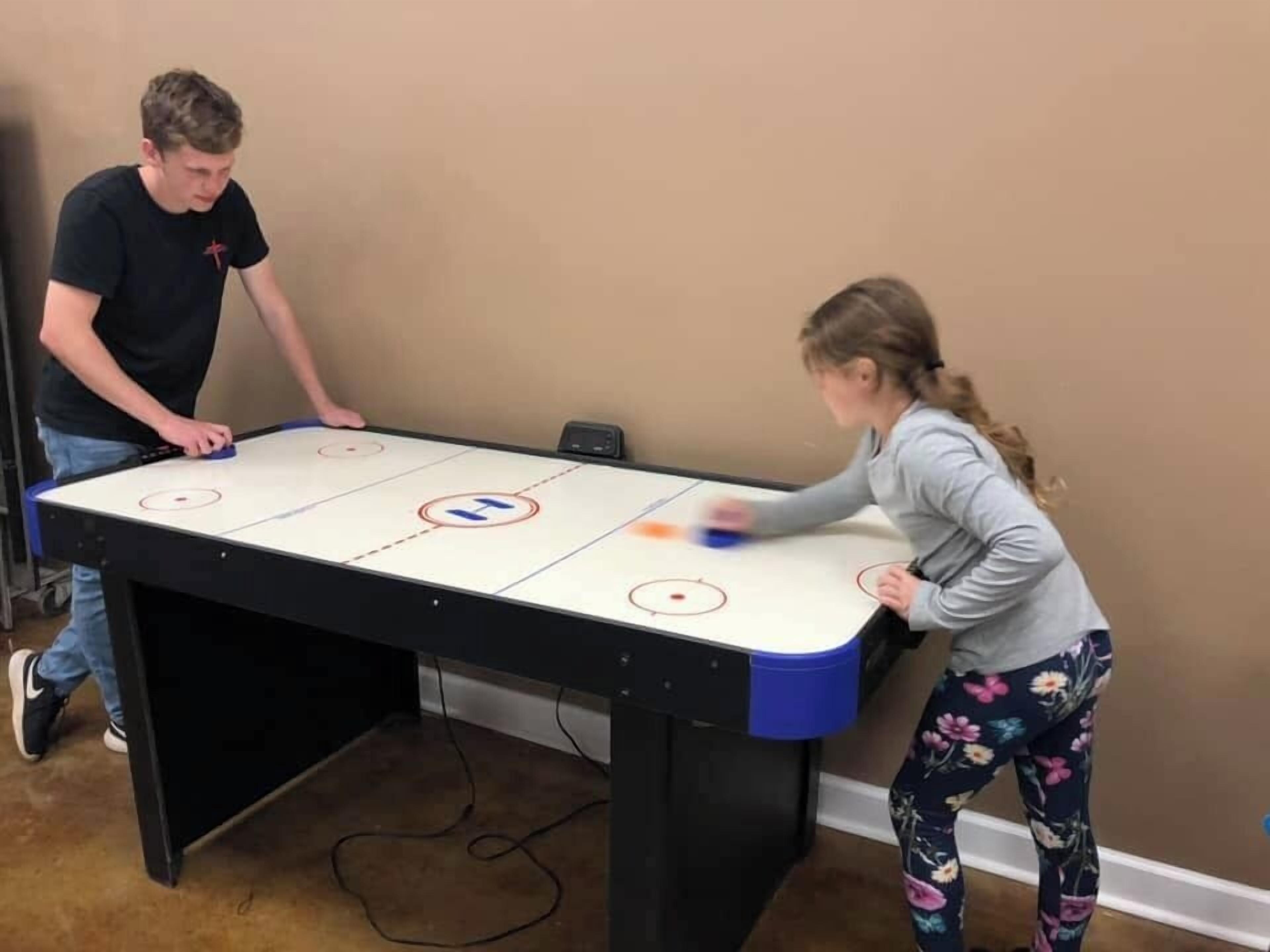 Two people playing table hockey on a table with a hockey puck and a stick.